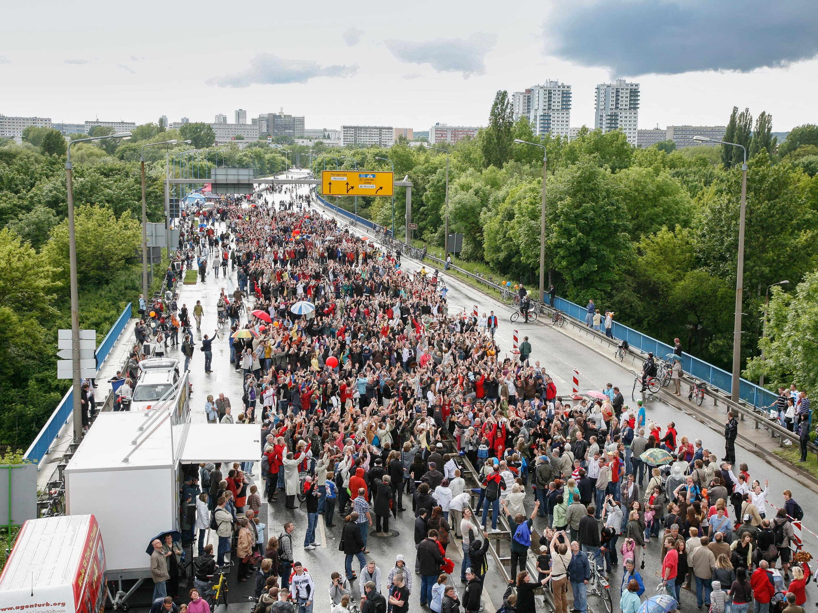 Das Bild zeigt eine Luftaufnahme der halleschen Hochstraße, einer mehrspurigen Hauptverkehrsstraße. Sie ist überfüllt mit Menschen, welche anlässlich der Aktion "autofreier Tag" auf der Hochstraße spazieren gehen.