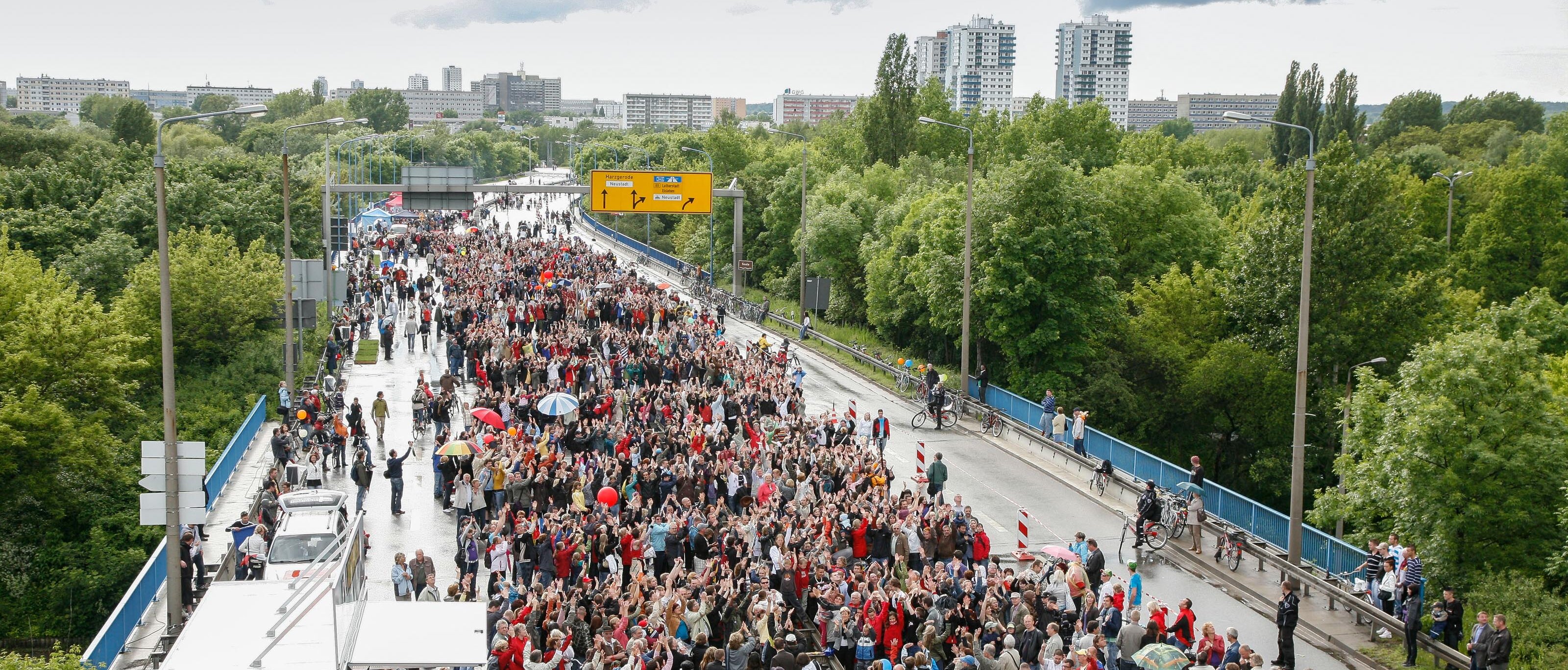Das Bild zeigt eine Luftaufnahme der halleschen Hochstraße, einer mehrspurigen Hauptverkehrsstraße. Sie ist überfüllt mit Menschen, welche anlässlich der Aktion "autofreier Tag" auf der Hochstraße spazieren gehen.