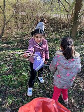 3 Kinder der Kita sammeln Müll ein, im Vordergrund ist der Müllsack zu sehen. 