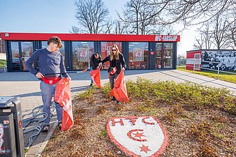 3 Personen sammeln Streumüll vor dem HFC-Fanshop ein. 