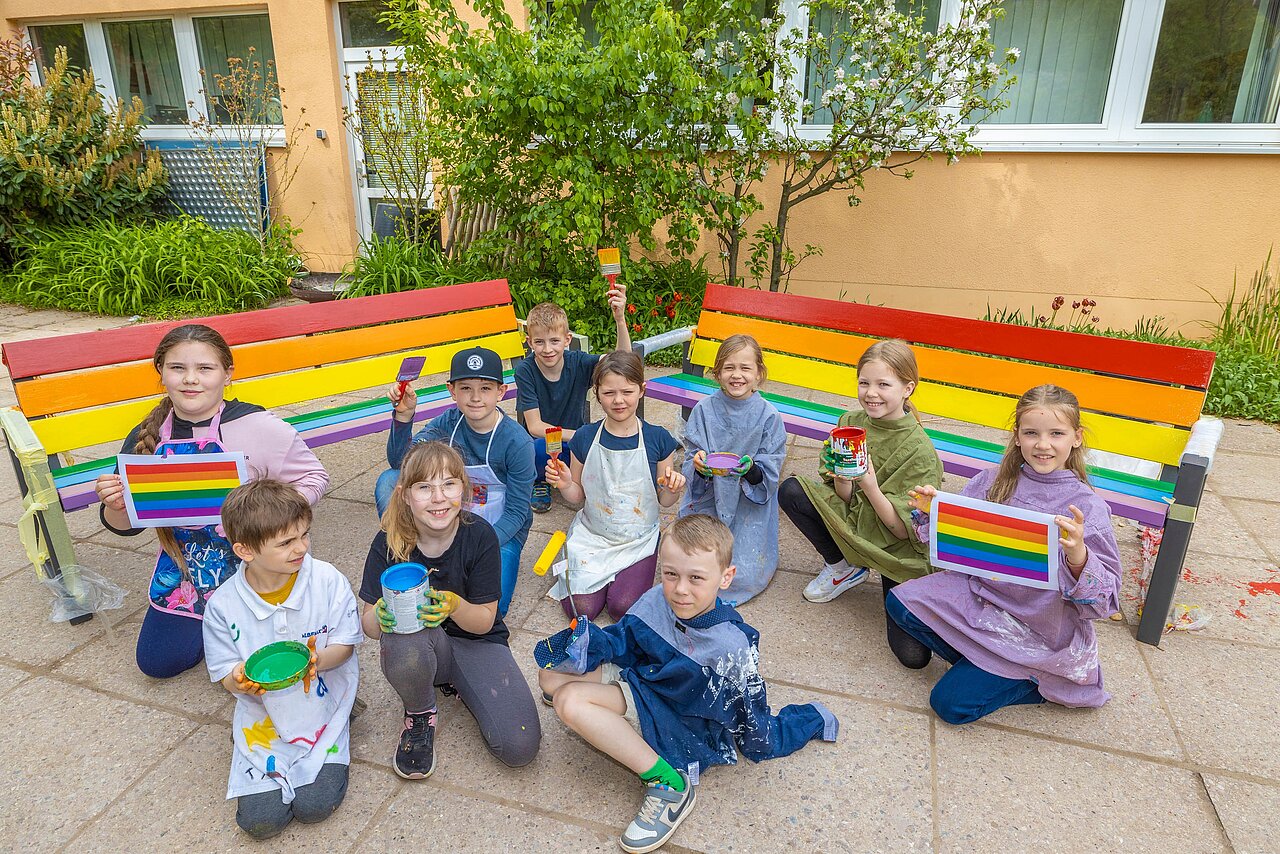 Eine Gruppe Schülerinnen und Schüler vor zwei Bänken die in Regenbogenfarben bemalt wurden