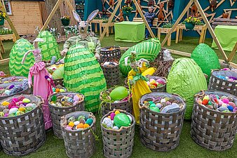 Osterhasen und große grüne Ostereier hinter Körben voller Ostereier