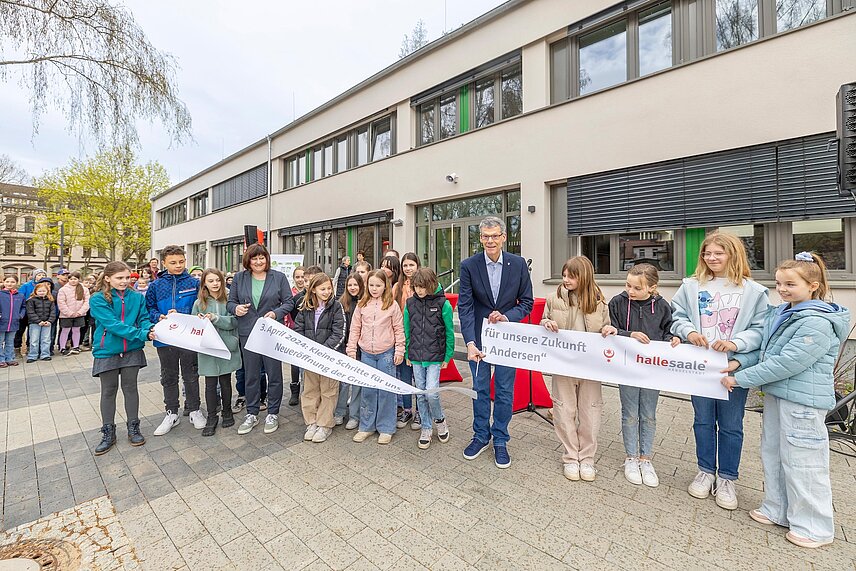 Bürgermeister Egbert Geier und Schulleiterin Bianca Kutzner sowie Schülerinnen und Schüler durchschneiden bei der Eröffnung der sanierten Grundschule „Hans-Christian Andersen“ in Trotha das Band durch.   