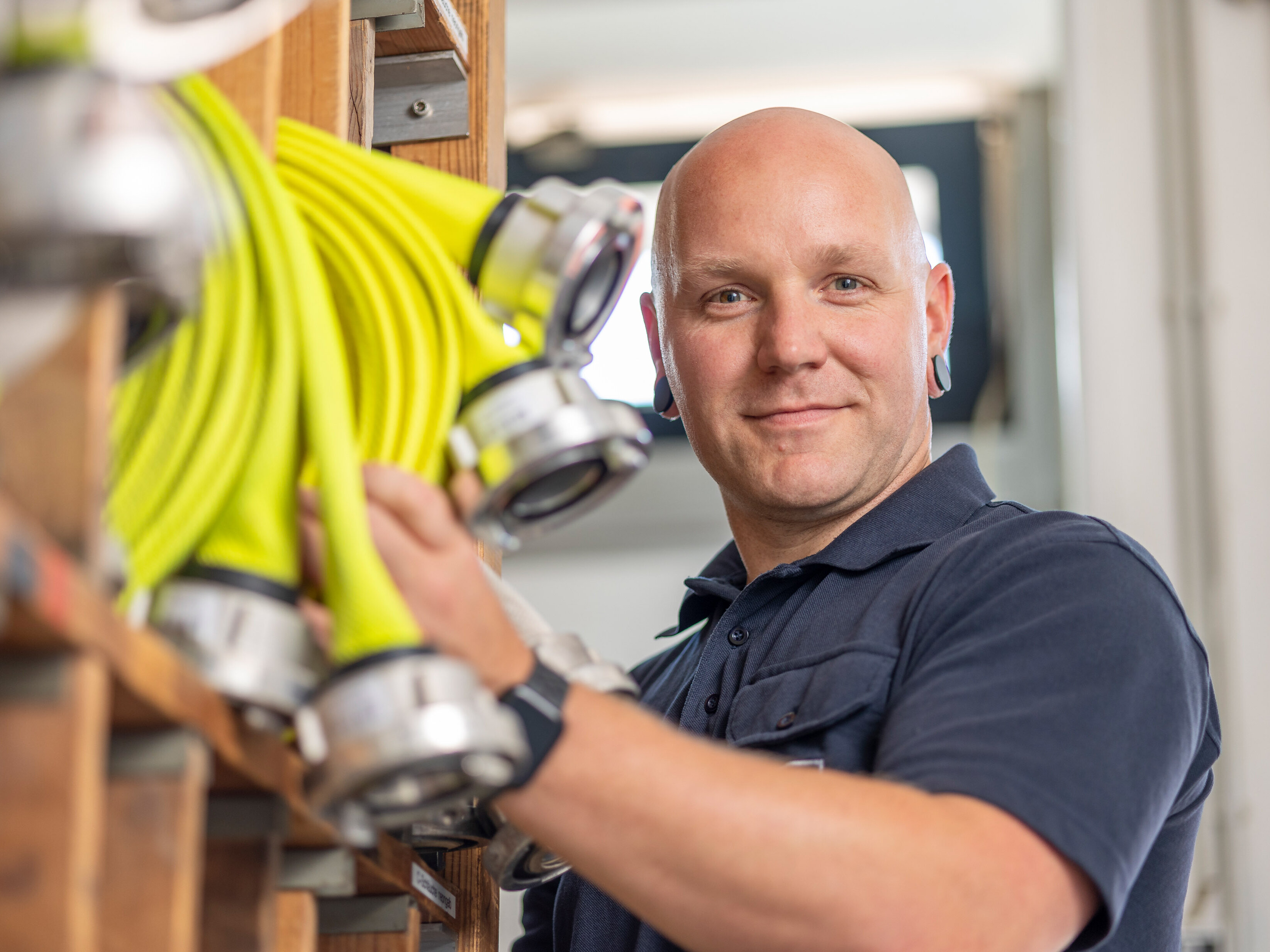 Christian Fincke, Brandmeister bei der Berufsfeuerwehr Halle (Saale), er ist in der Werkstatt der Feuerwehr und hat einen Löschschlauch in der Hand.