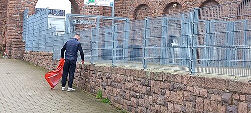 Eine Person sammelt Streumüll mit einer Greifzange auf.