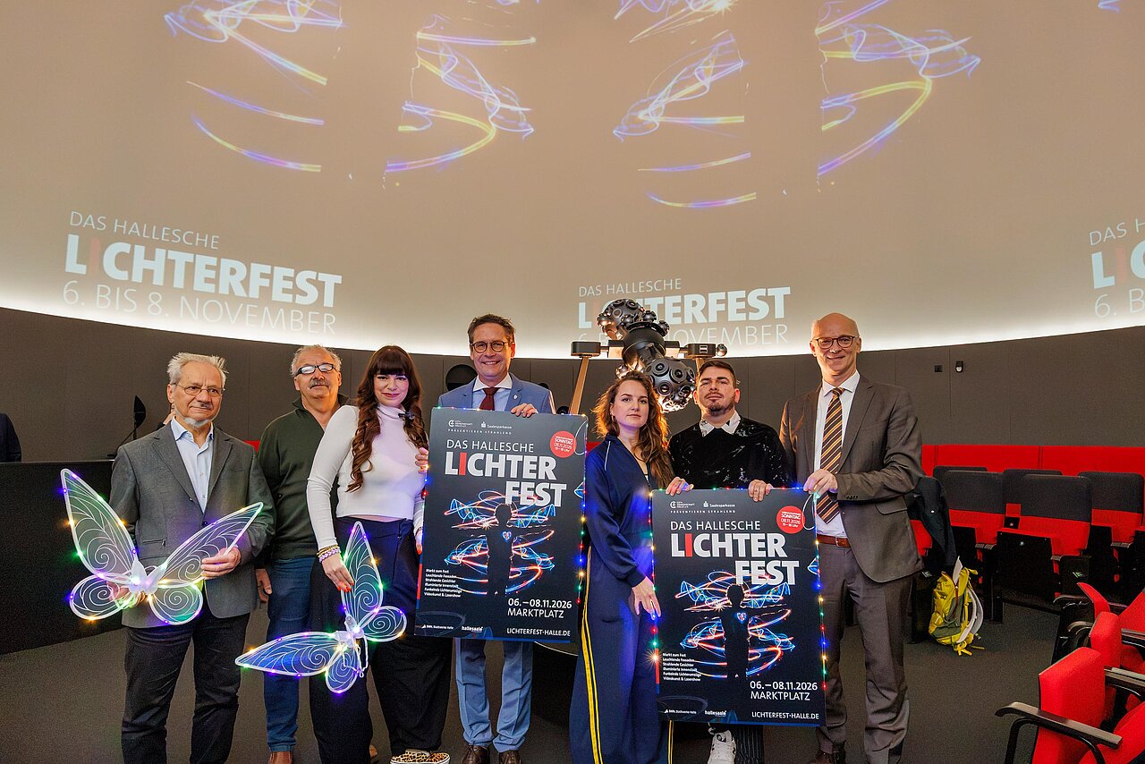 Gruppe von sieben stehenden Personen, die im Planetarium Lichterfest-Plakate und Leuchtelemente zeigen. 