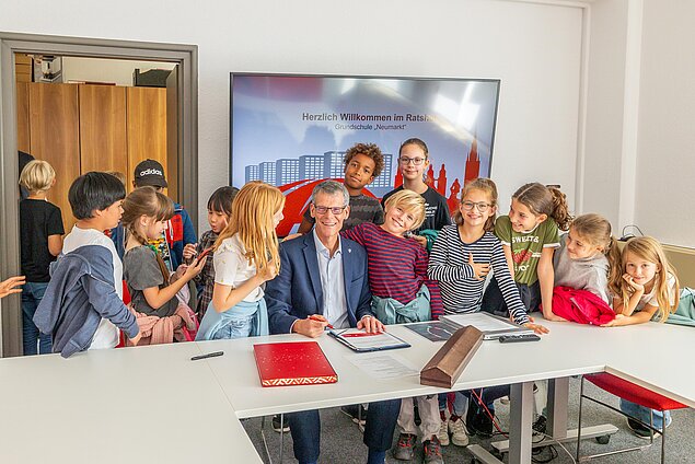 Gruppenfoto am Tisch mit Bürgermeister und Kindergruppe.