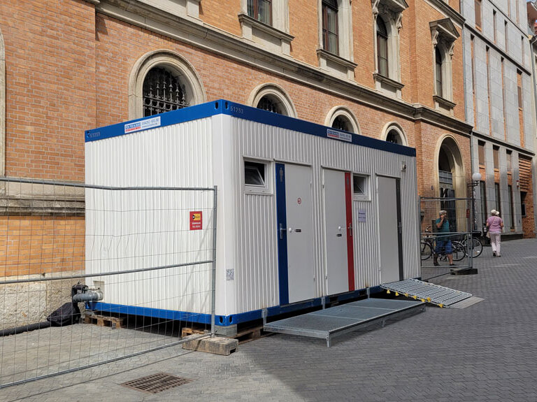weißer Toilettencontainer in der Rathausstraße vor dem Stadtarchiv mit 3 Türen für männlich, weiblich und behindert mit Rollstuhlrampe