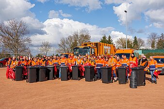 Zahlreiche Mitarbeitende der Stadtwerke stehen versammelt mit Müllsäcken und Mülltonnen vor einem Entsorgungsfahrzeug. 