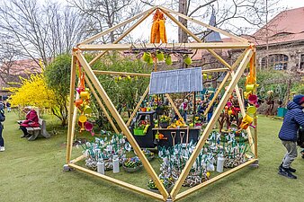 Holzbalken zu einer Art Gewächshaus gebaut mit gebastelten Blumen, Gießkannen u.a. gestaltet