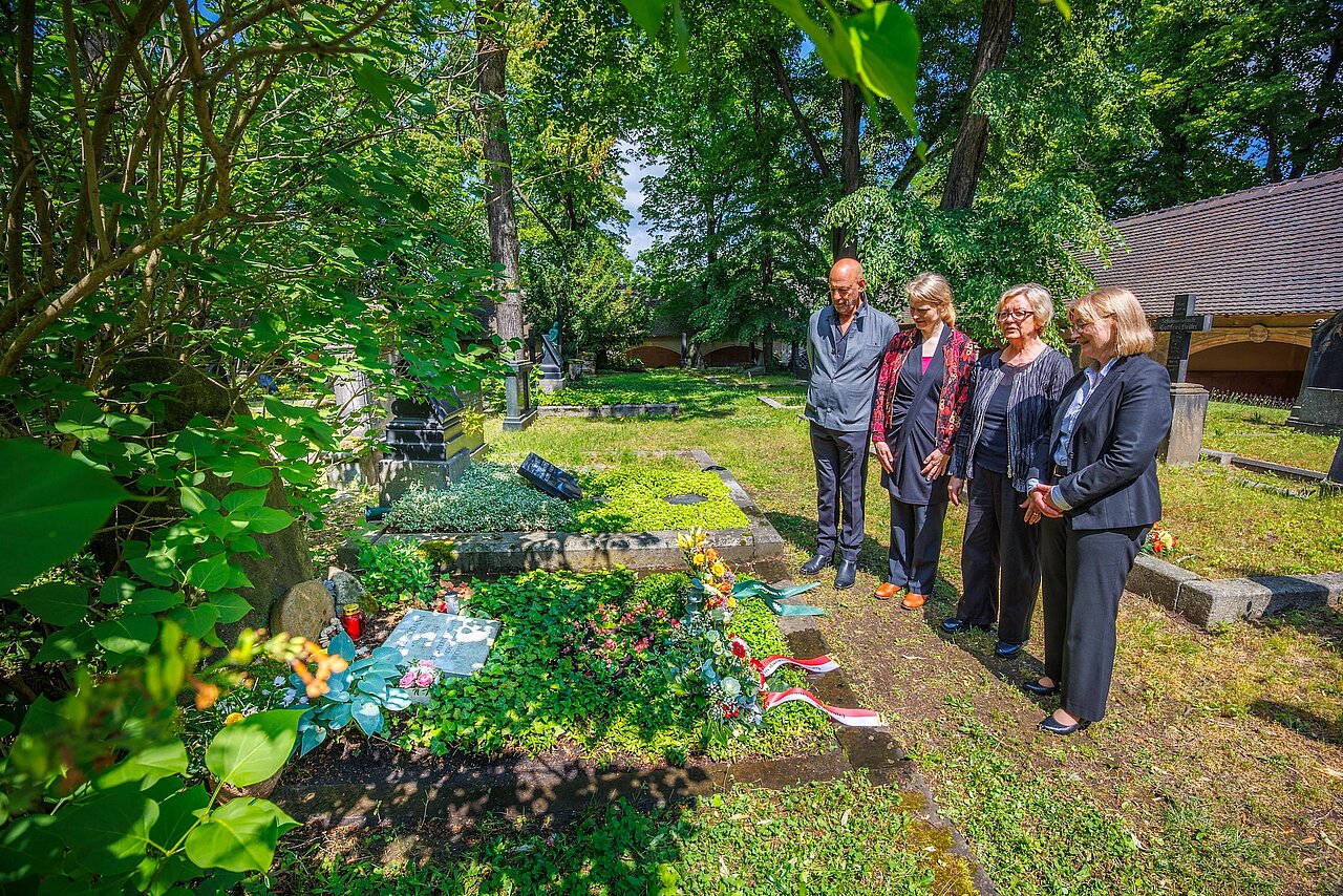 Vier Personen im stillen Gedenken an einem geschmückten Grab  