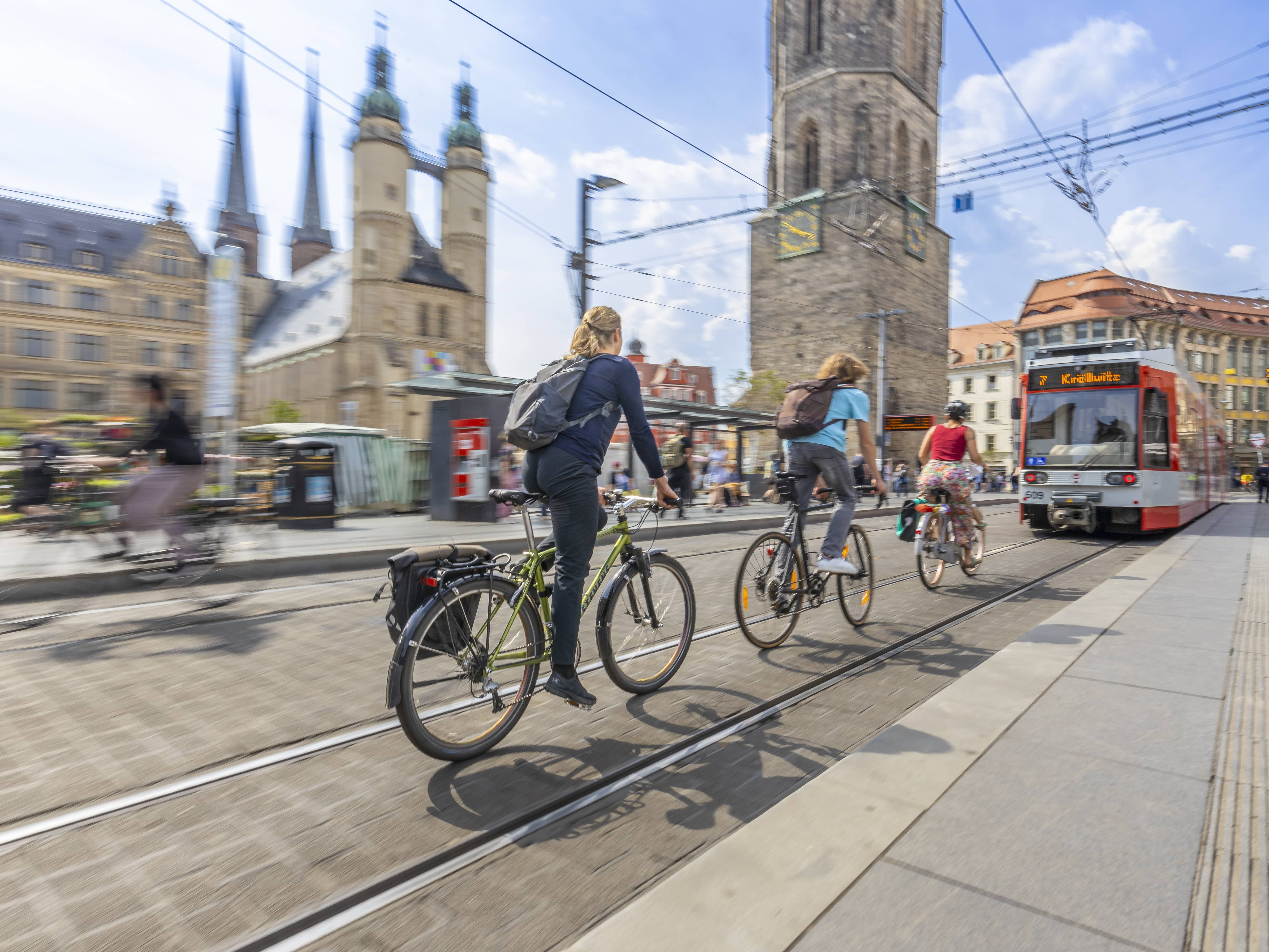 Fahrradfahrer von hinten sichtbar auf einer Straße zwischen einem Gleisbett hinter einer Straßenbahn fahrend