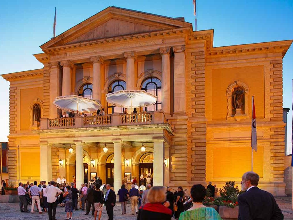 Der prächtige Eingang des Opernhauses, wartende Menschen davor an einem Sommerabend