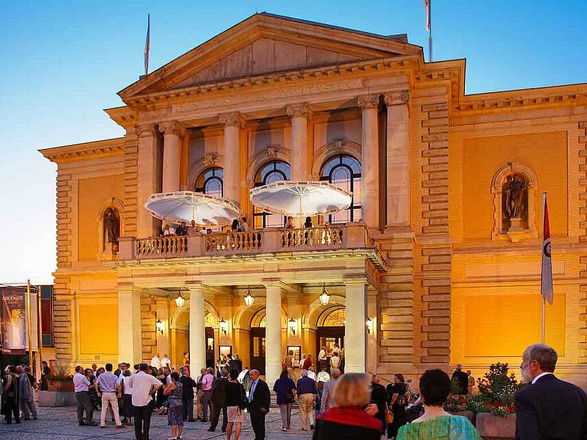 Der prächtige Eingang des Opernhauses, wartende Menschen davor an einem Sommerabend