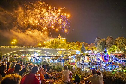 Vom Saaleufer blicken Besucher in den Himmel.