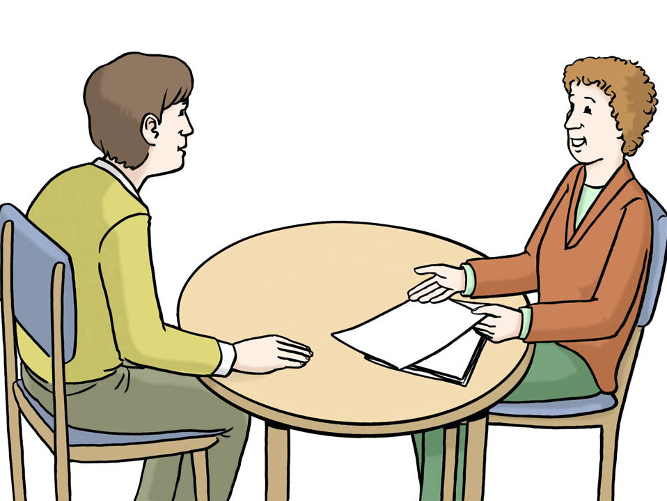 Zwei Personen sitzen an einem Tisch. Eine Person hat mehrere Blätter und einen Stift in der Hand und erklärt. Die andere Person hört zu.