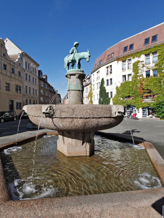 Junge mit Esel auf einer Säule, darunter aus Stein Brunnenschale mit Fischköpfen