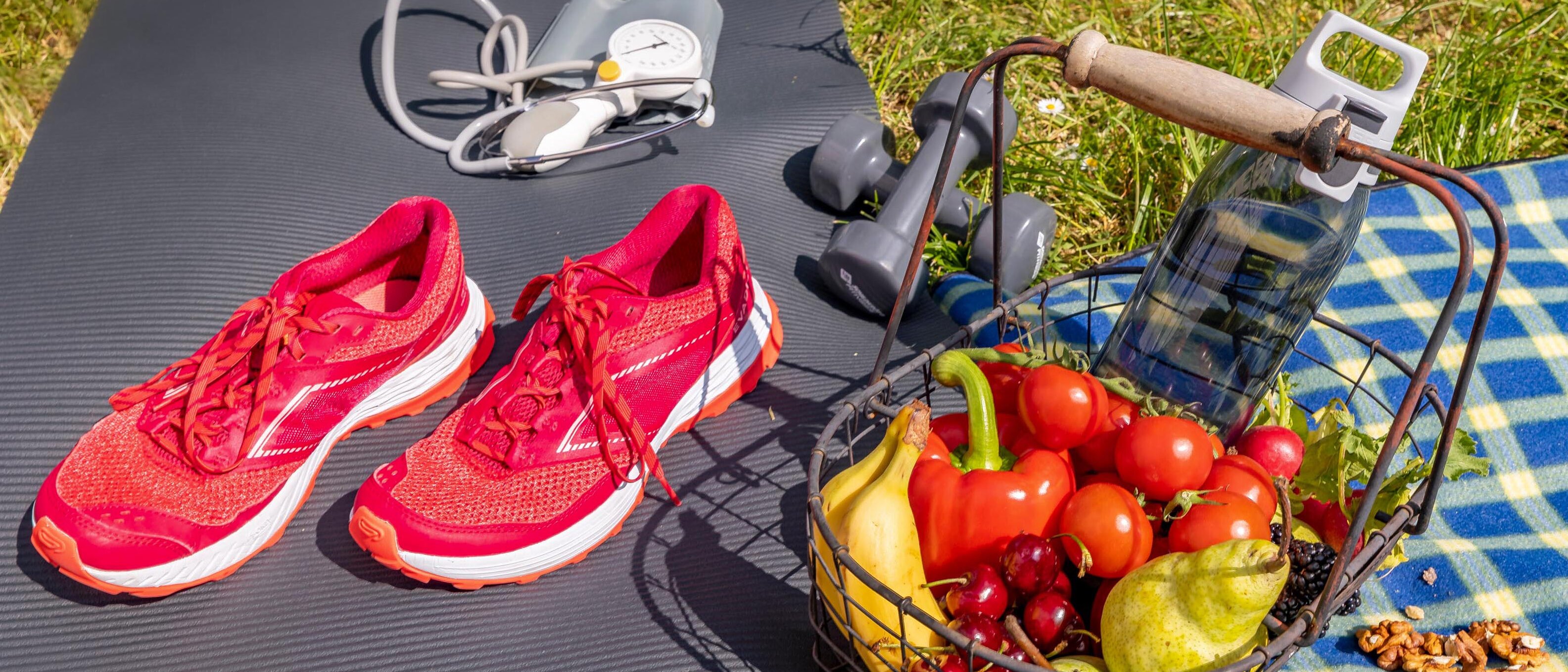 Yogamatte und Picknickdecke mit Laufschuhen, Stethoskop sowie Obst- und Gemüsekorb und Wasserflasche