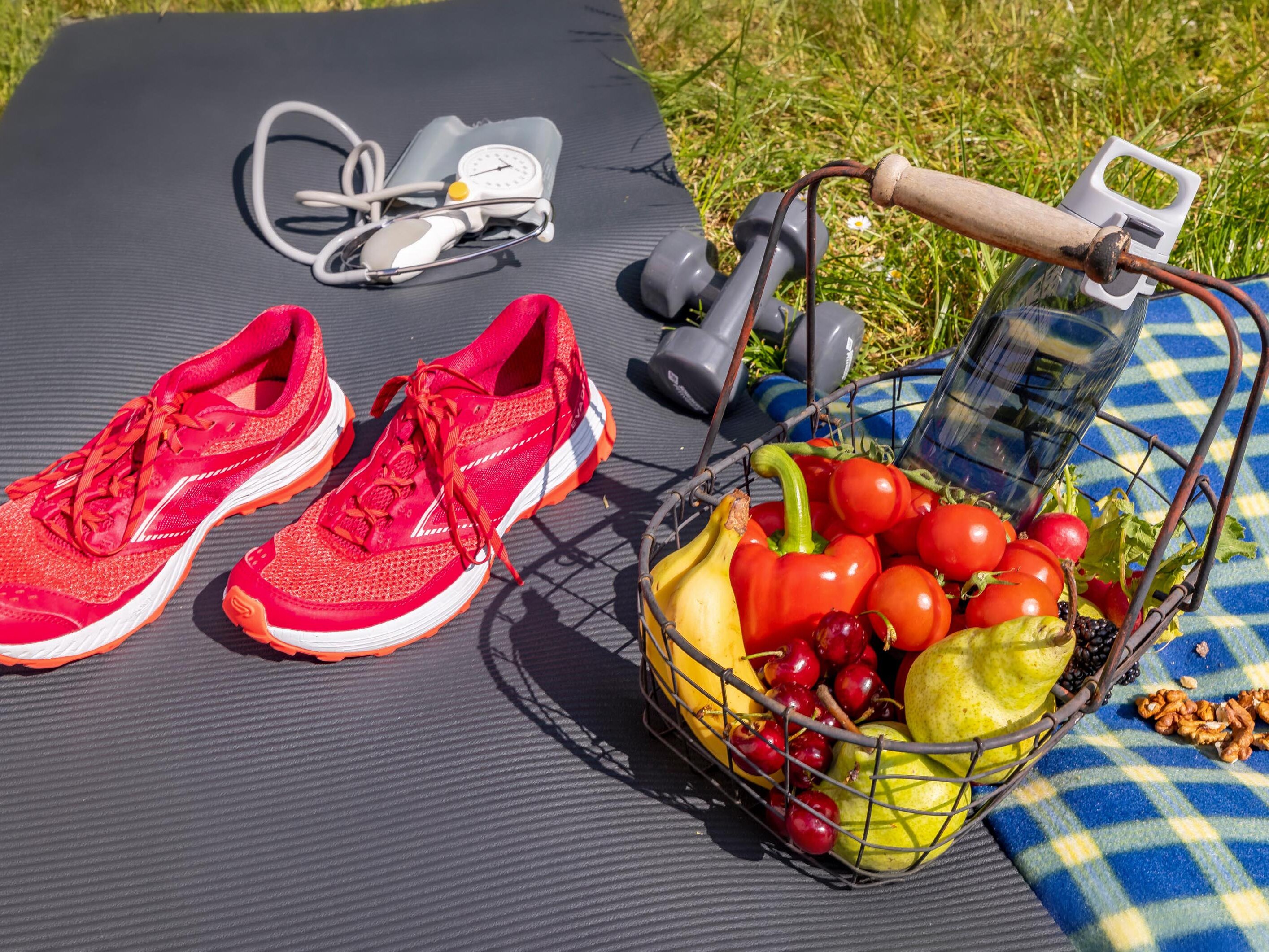 Yogamatte und Picknickdecke mit Laufschuhen, Stethoskop sowie Obst- und Gemüsekorb und Wasserflasche