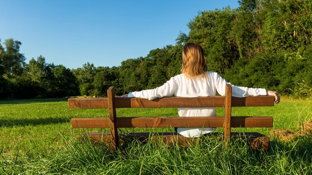 Eine Frau sitzt auf einer Bank und schaut in die grüne Umgebung.