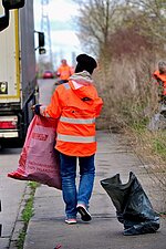 Mitarbeitender der Stadtwerke trägt einen Müllsack am Straßenrand entlang.
