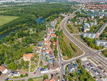 Blick über den dörflichen Stadtteil Wörmlitz mit Kirche in Richtung Norden, westlich erstreckt sich die grüne Saaleaue bis zur Rabeninsel, durch eine breite Strasse getrennt von der Altbebauung stehen rechts mehrgeschossige Neubauten der Südstadt von Halle