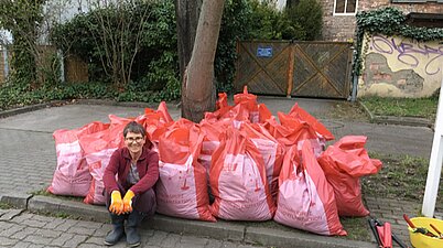 Eine Frau sitzt vor befüllten Müllsäcke auf dem Bordstein.
