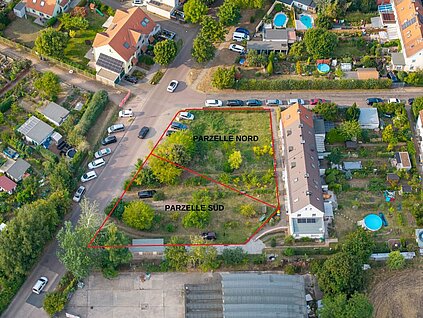 Luftansicht einer Grünfläche an einer Straßenkreuzung mit vorhandener Wohnbebauung, die möglichen Bauparzellen sind markiert