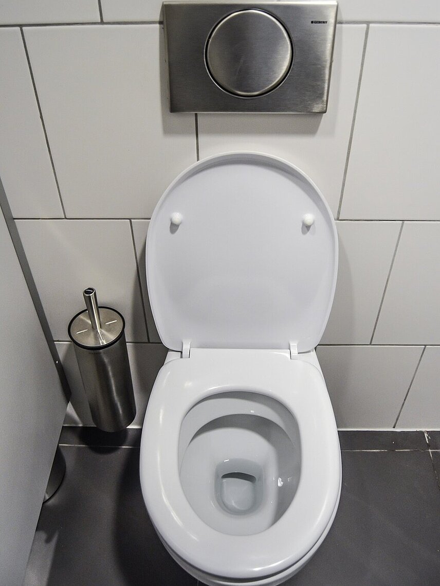 eine offene Toilette mit weißer Brille in einem weißen Bad