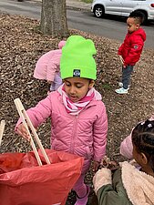 Kind einer Kita sammelt Müll mit Holzzange ein.