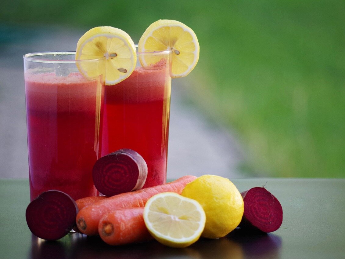 Zwei Gläser roter Gemüsesaft (Rote Bete) mit Zitronenscheiben; daneben Möhren, Rote Bete und Zitrone.