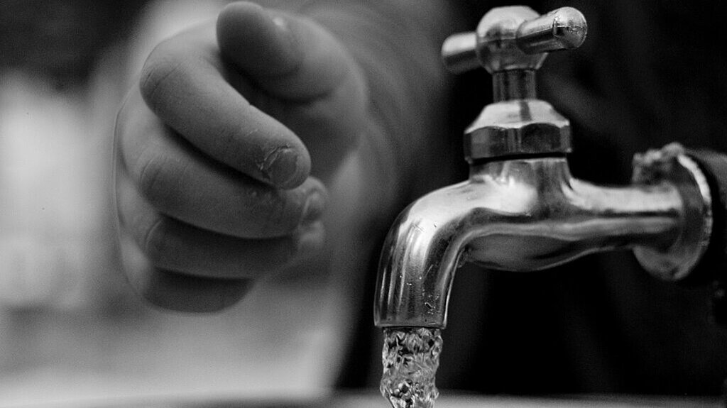 Trinkwasser fließt aus dem Wasserhahn und eine Hand greift danach