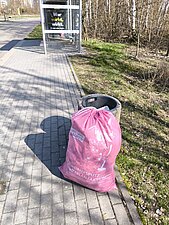 Ein befüllter Müllsack steht neben einem Papierkorb.