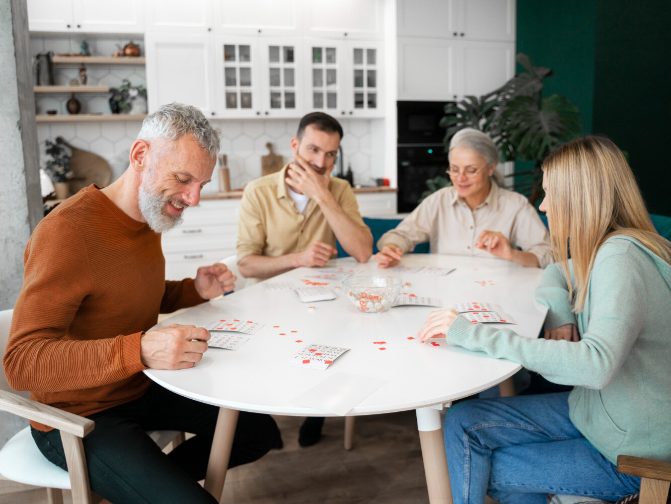 Vier Menschen verschiedener Generationen sitzen gemeinsam an einem Tisch und spielen ein Gesellschaftsspiel.