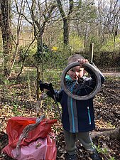 Ein Junge hält ein einzelnes (Schrott-)Rad hoch und hält eine Greifzange in der anderen Hand.