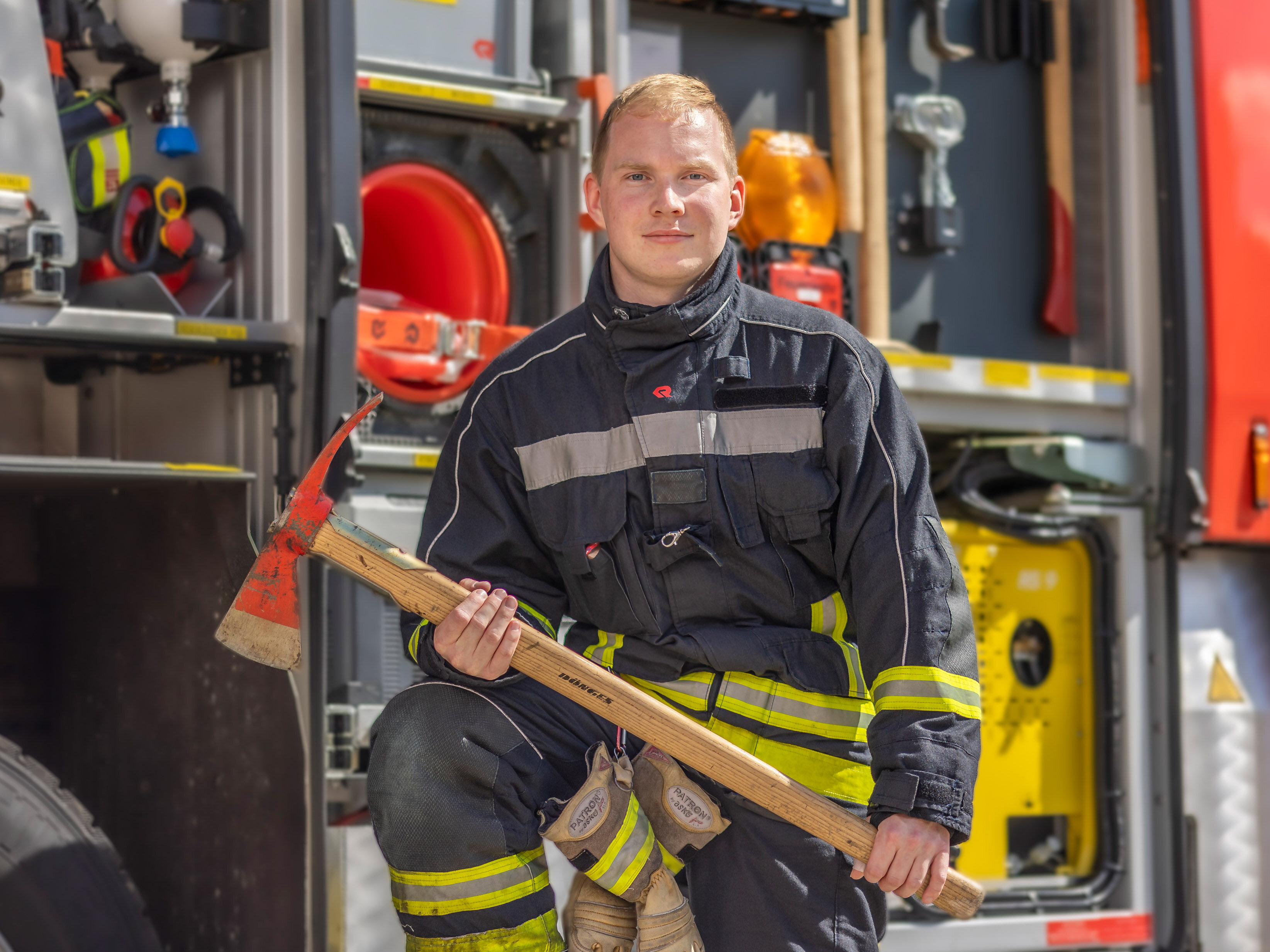 Jonathan Hesse, Brandmeister bei der Berufsfeuerwehr Halle (Saale), er steht vorm Einsatzfahrzeug und hat eine Axt in der Hand 