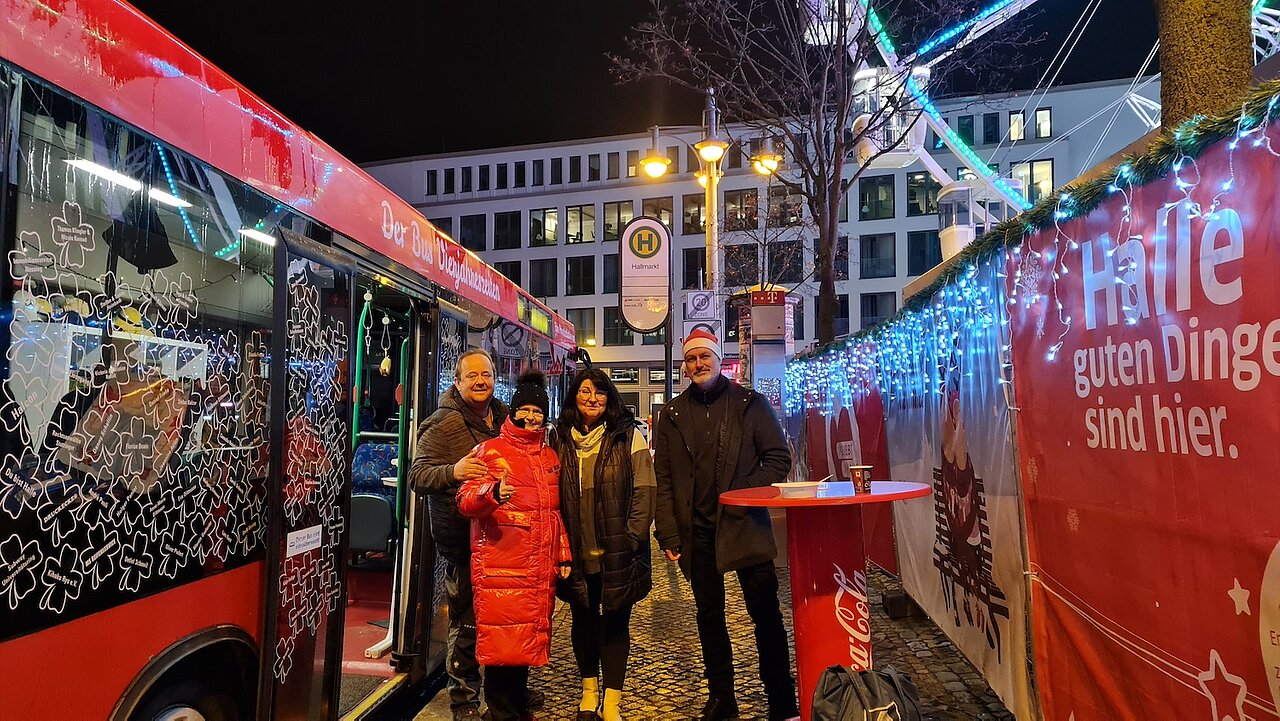 Vier Personen stehen am Hallmarkt neben einem Bus mit geöffneten Türen