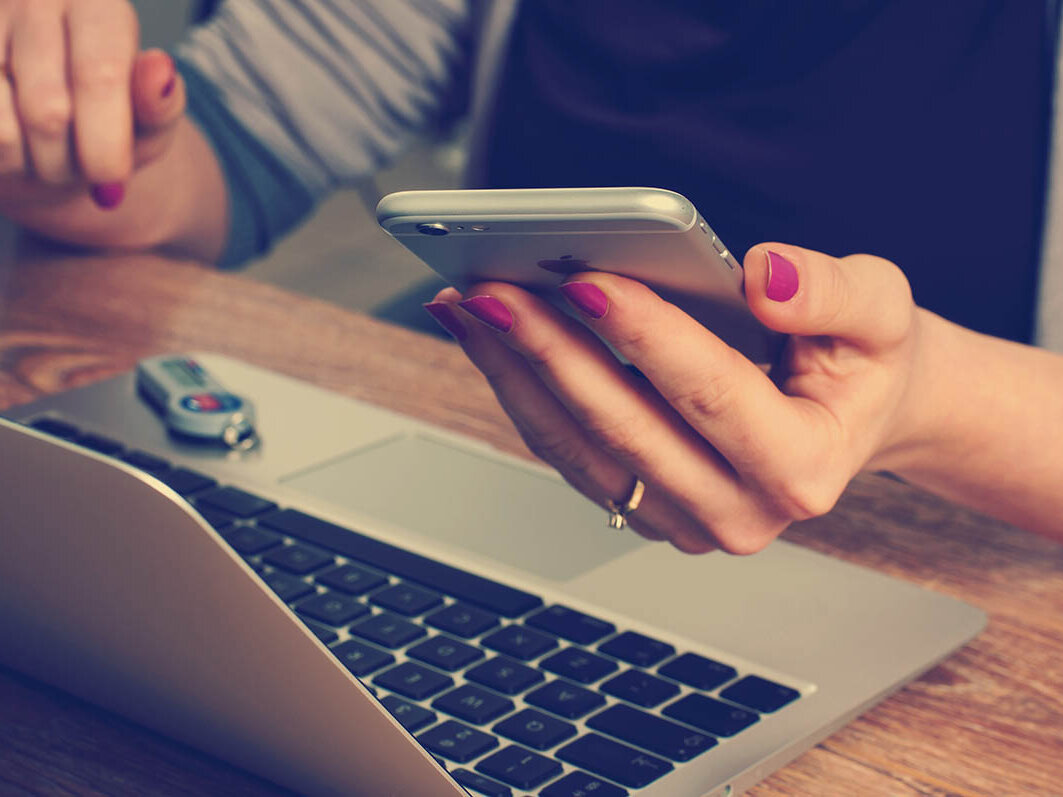 Frauenhände mit einem Smartphone in der Hand vor einem Laptop