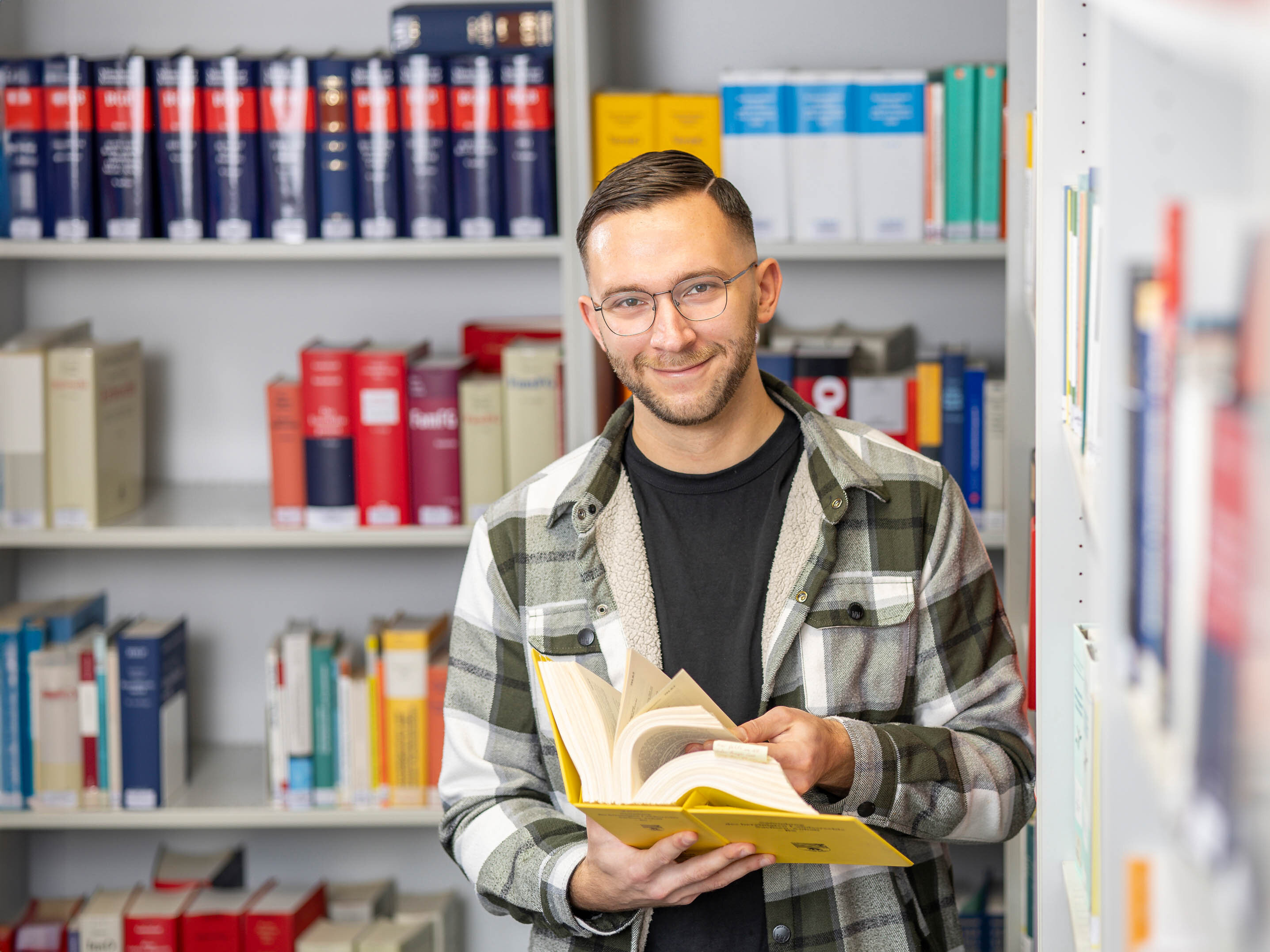 Tim Richter, dualer Student der öffentlichen Verwaltung bei der Stadtverwaltung Halle (Saale), vor einem Bücherregal in der Bibliothek