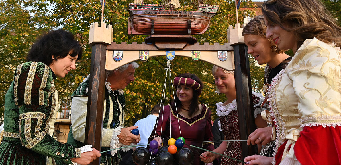 Menschen mit historischen Kostümen stehen um eine hängende Kogge