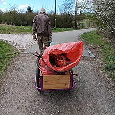 Ein Mann zieht einen Anhänger hinter sich her, auf dem sich Müllsäcke und Greifzangen befinden.