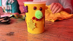 ein Joghurtbecher mit grünen Stoff und einem Gesicht beklebt