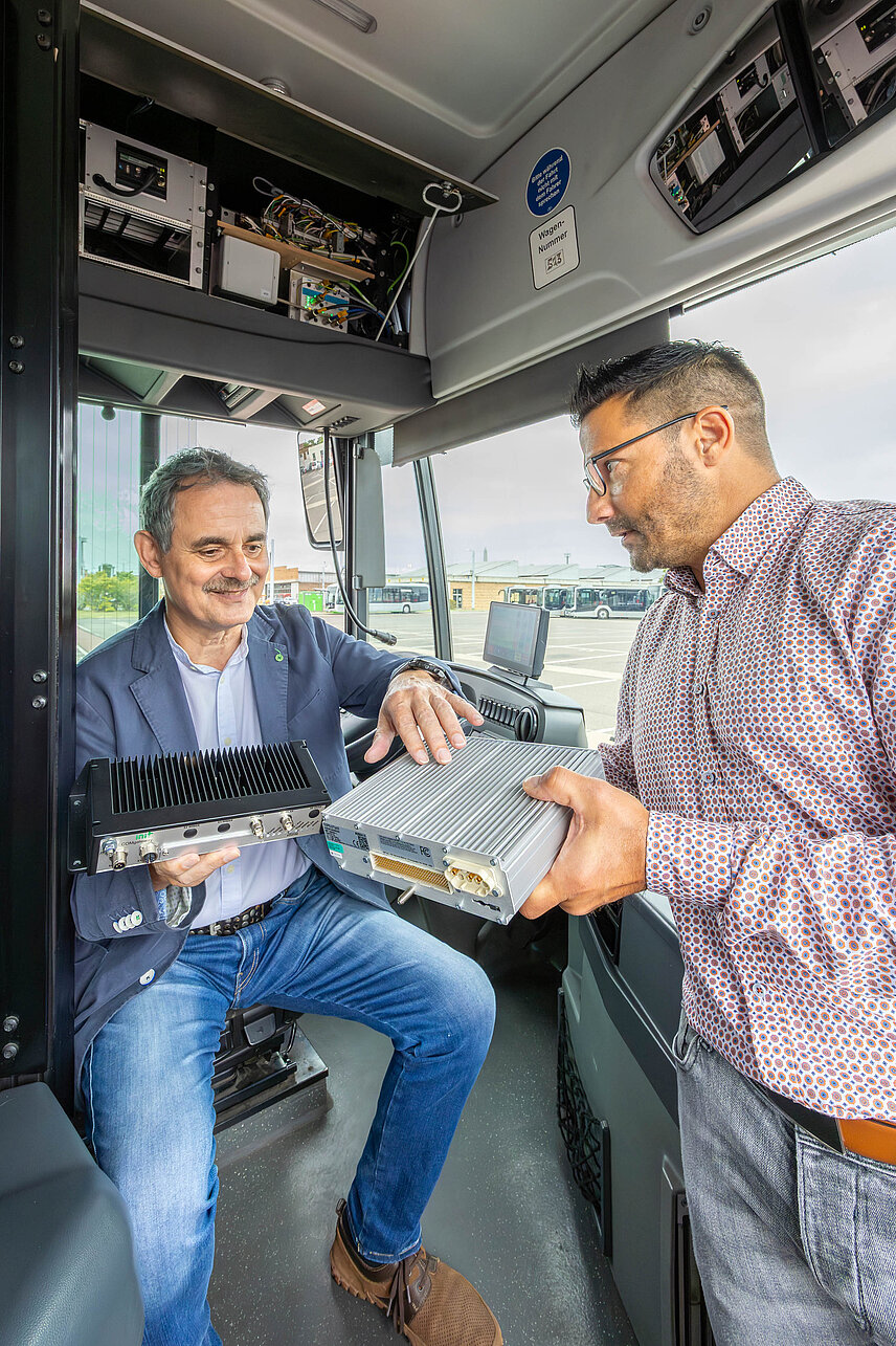 Zwei Männer im Fahrerstand eines Busses, die sich die neue Technik in Form eines Kastens ansehen