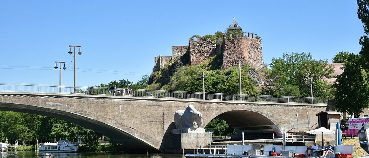 Burgruine am Flussufer, Bogenbrücke mit Pferdskulptur, Boote und Kanu auf dem Wasser