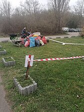 Foto zeigt einen Haufen mit befüllten Müllsäcken und im Hintergrund eine Person, die mit einem kleinen Anhänger fährt.