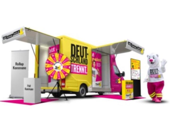 ein gelber Transporter mit Aktionsflächen und ein weißer menschenhöher Plüschbär mit roter Hose