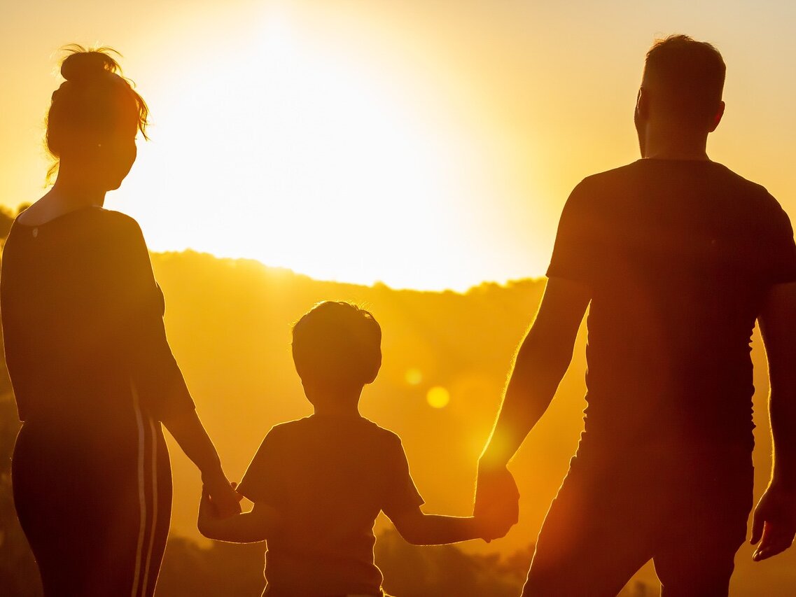 Eltern mit Kind von hinten vor Sonnenuntergang