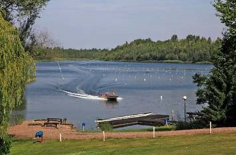 Blick auf die Regattastrecke des Osendorfer Sees. Ein Botorboot fährt am Ufer entlang 