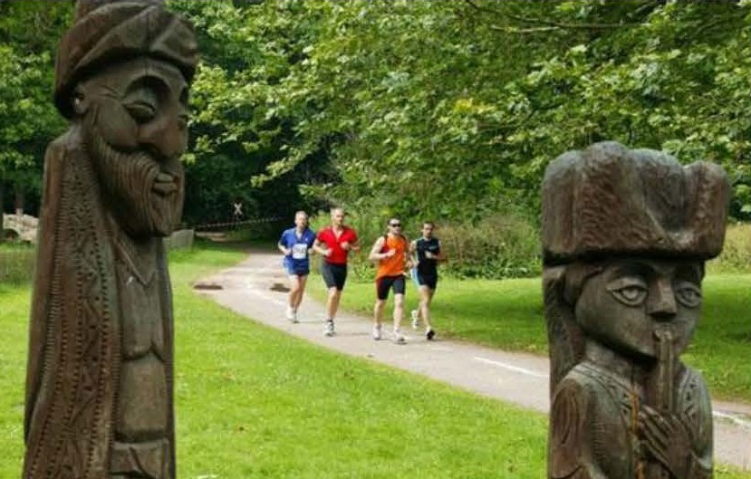 Laufgruppe von vier Läufern auf der Peißnitz. Rechts und Links neben der Laufgruppe steht jeweils eine Holz-Skulpturen  